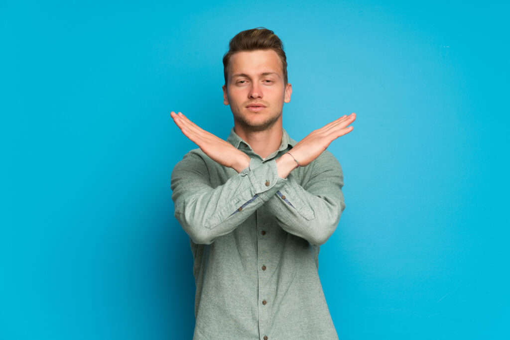 Blonde man over isolated blue wall making NO gesture