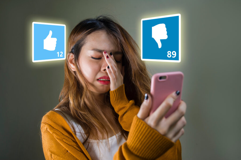 young cute and sad Asian Korean girl feeling unhappy and desperate holding mobile phone looking more dislikes than likes on her internet social media post in cyber bullying and influencer obsession