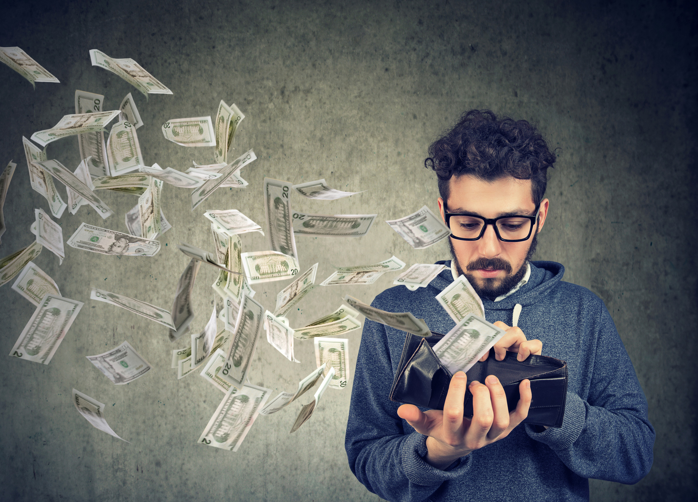 Sad man looking at his wallet with money dollar banknotes flying out away