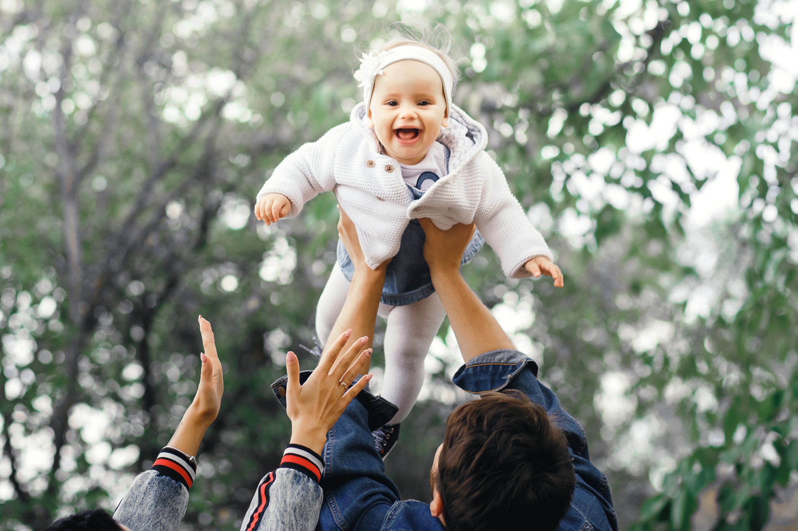 Happy family outdoors activity, father raises baby up, laughing and playing, father shows mother how to throws baby with safety.