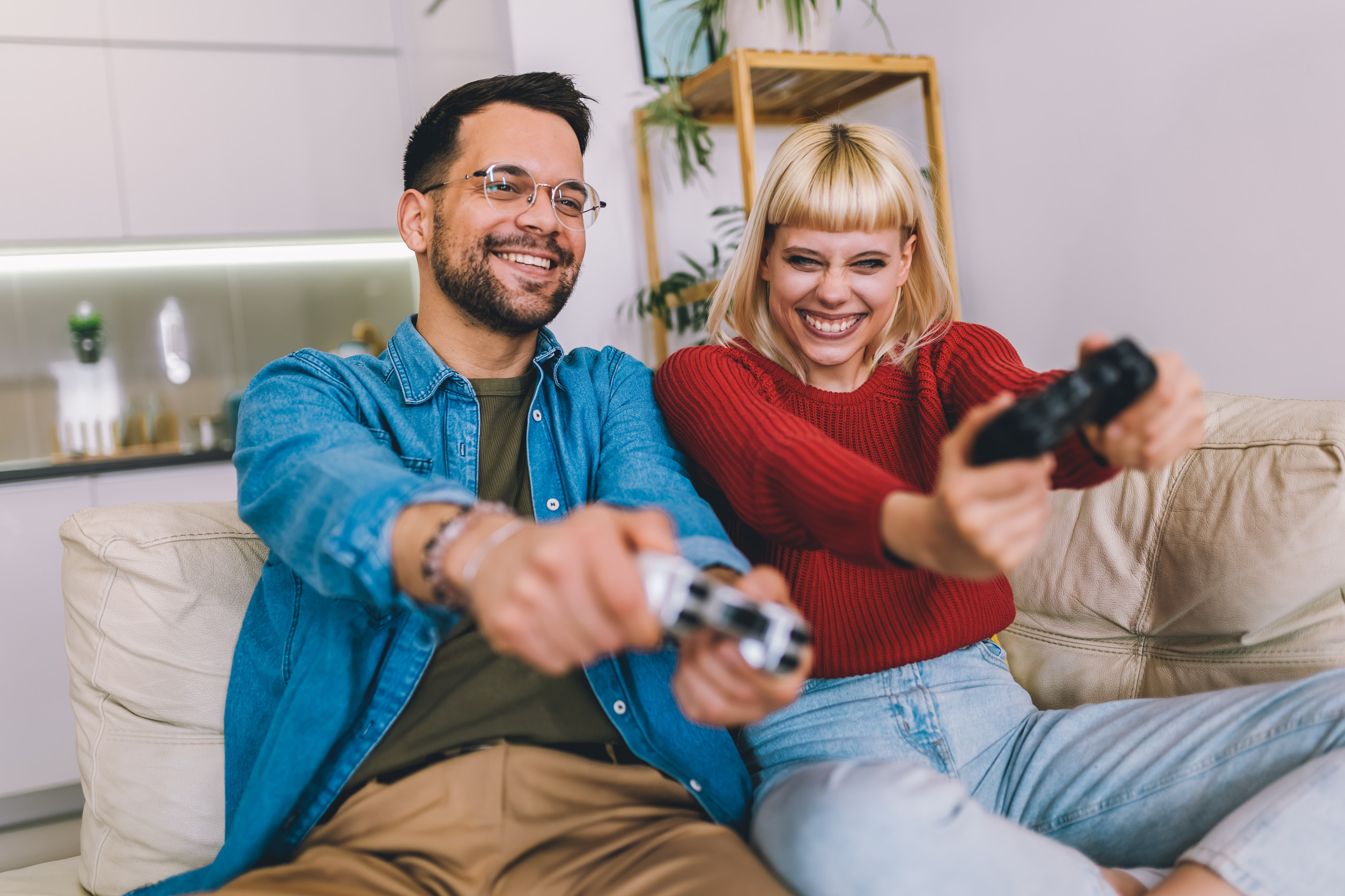 Boyfriend and girlfriend playing video game with joysticks in living room. Loving couple are playing video games at home.