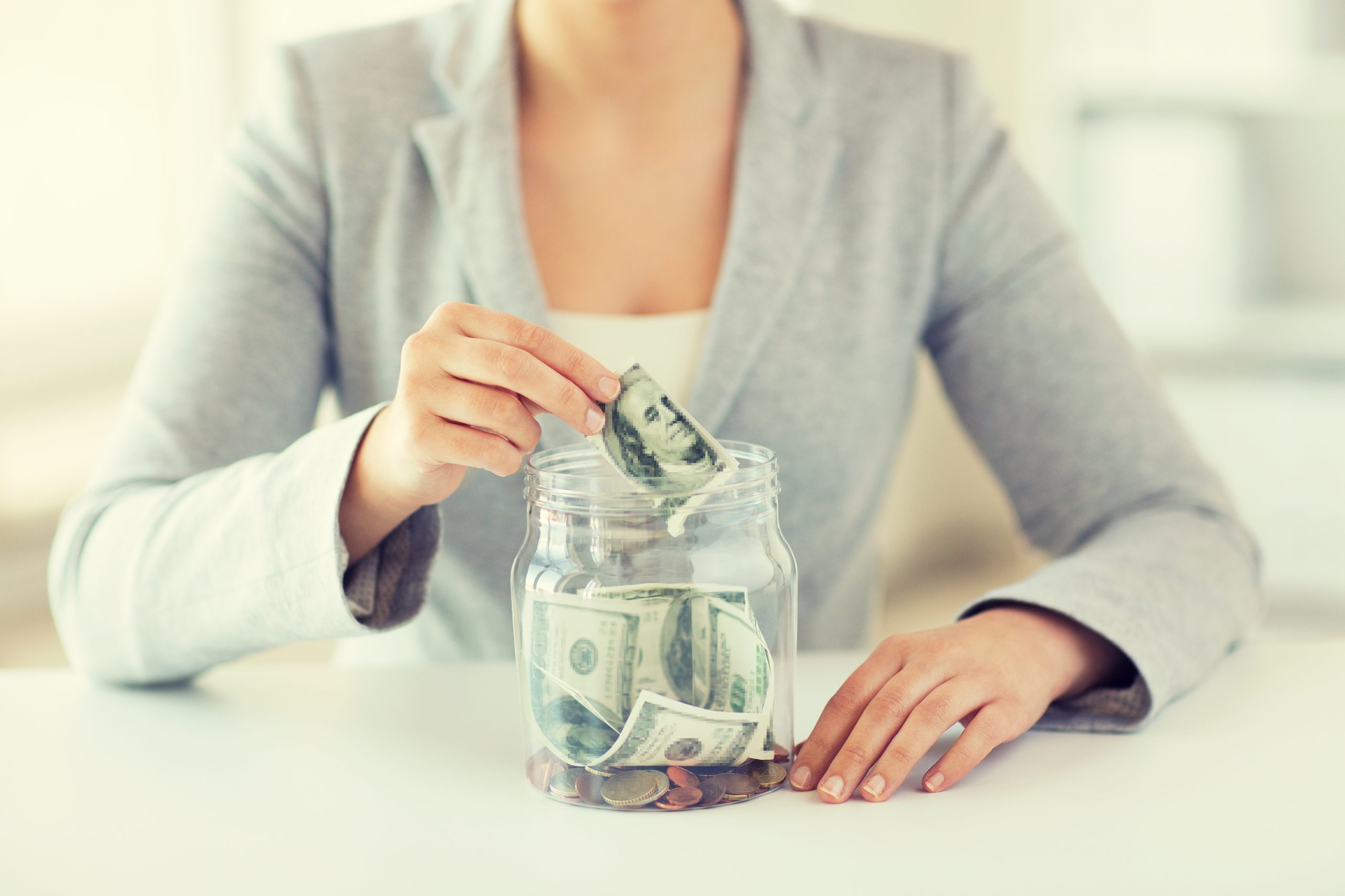 business, finance, saving, banking and people concept - close up of woman hands putting us dollar money into glass mason jar