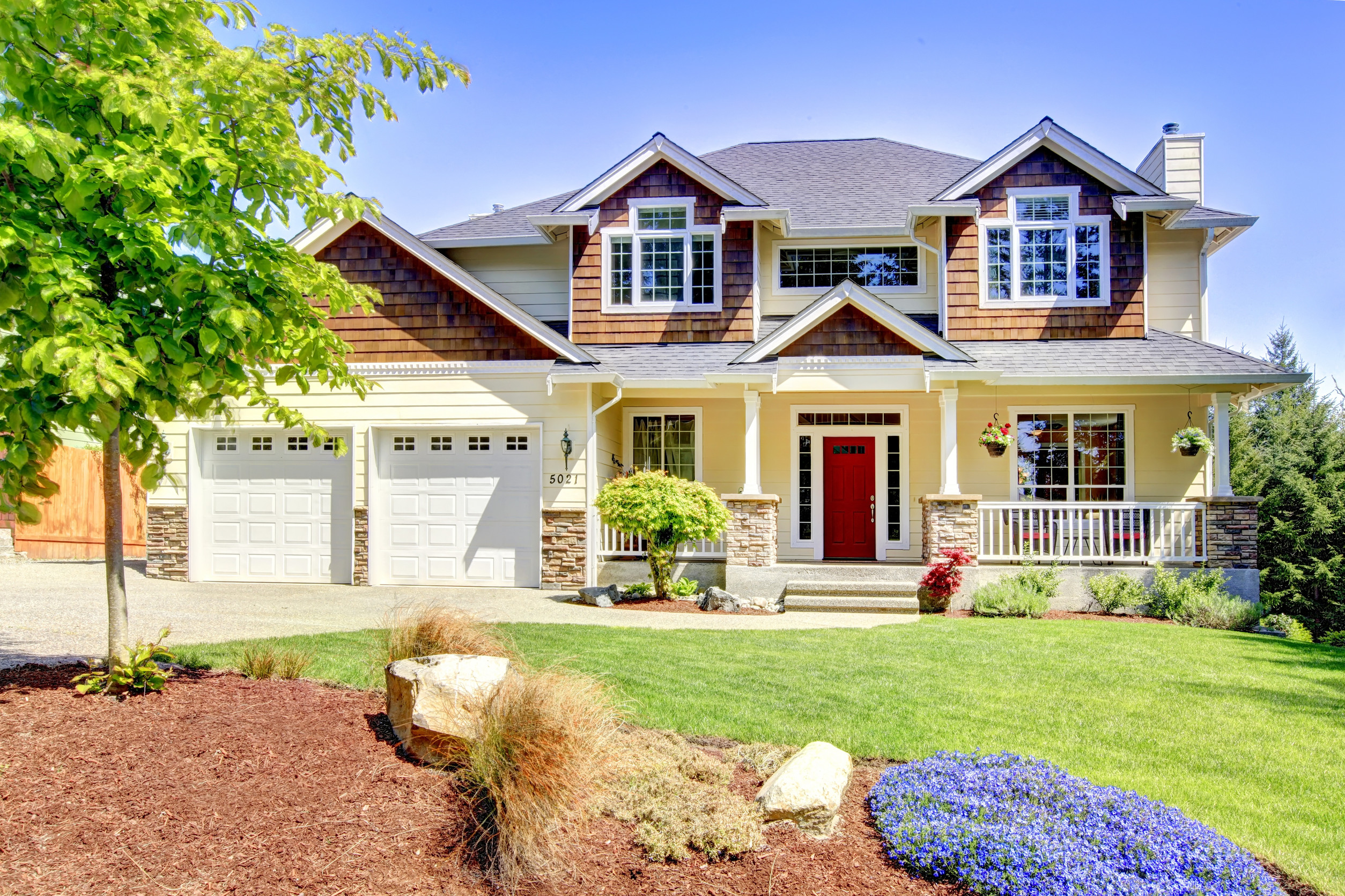 Large American beautiful house with red door and two white garage doors.