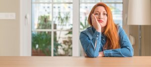 Redhead woman at home thinking looking tired and bored with depression problems with crossed arms.