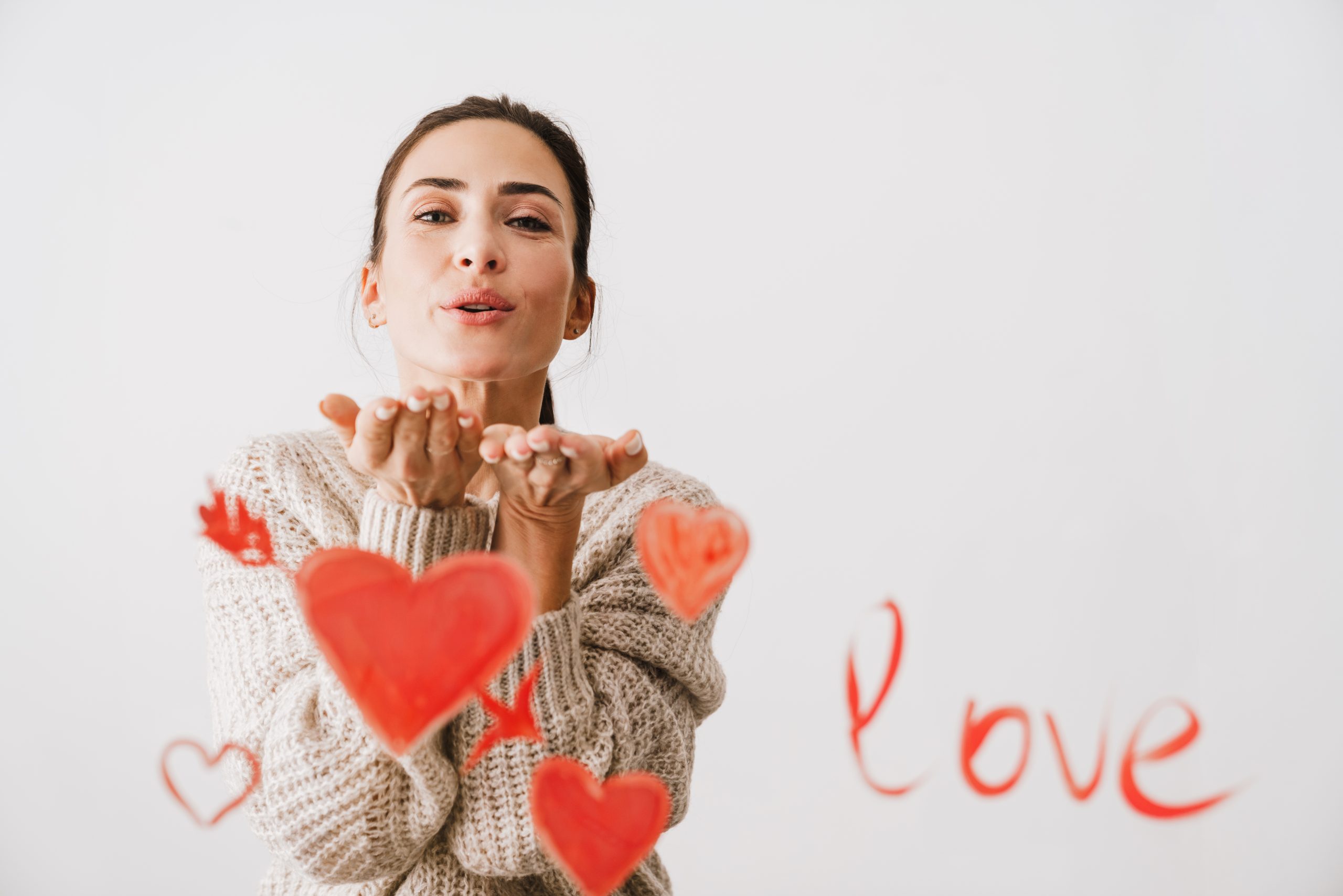 Beautiful smiling young woman in love drawing hearts in front of her isolated over white background, sending kiss, Valentines day concept