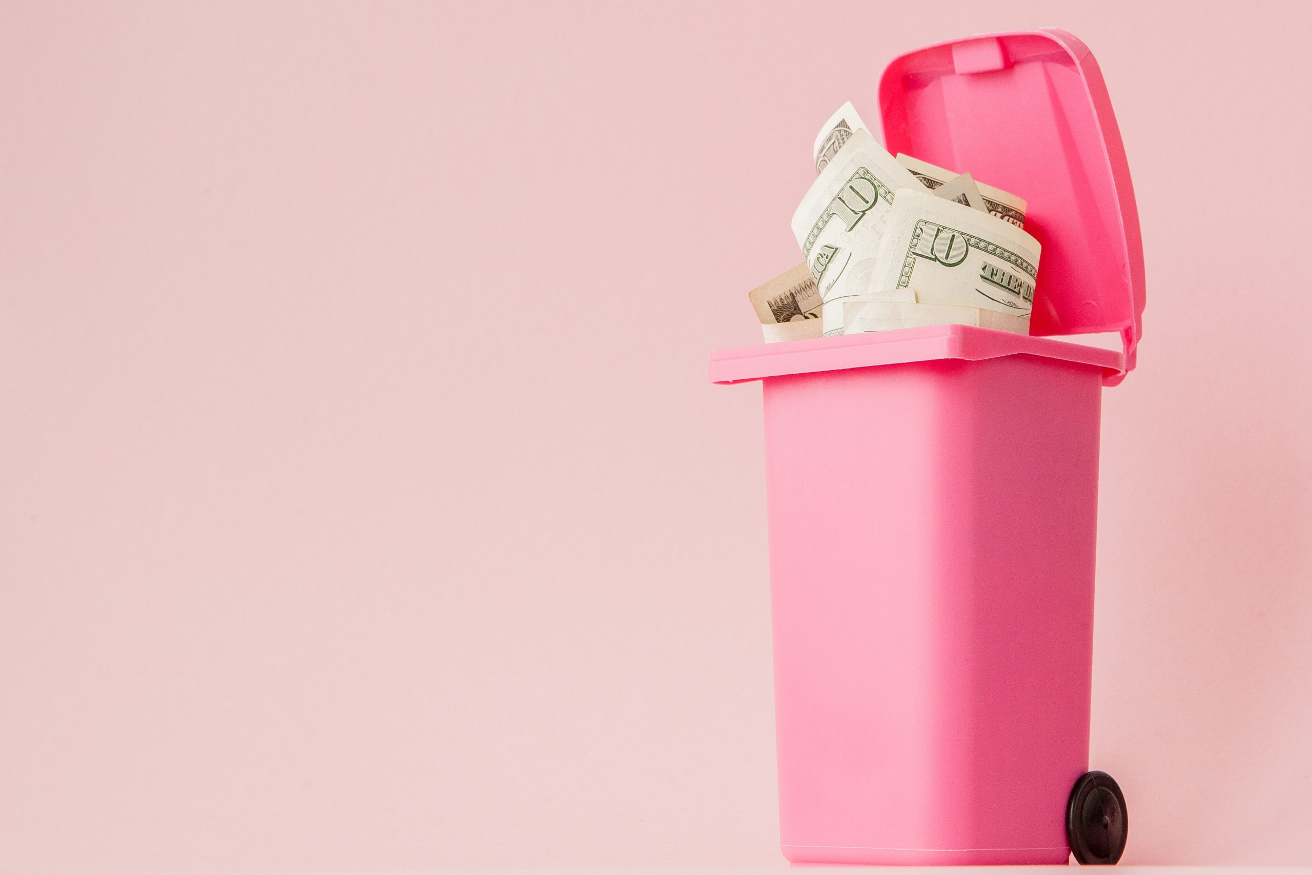 Dollars bank notes in pink rubbish bin on pink background.