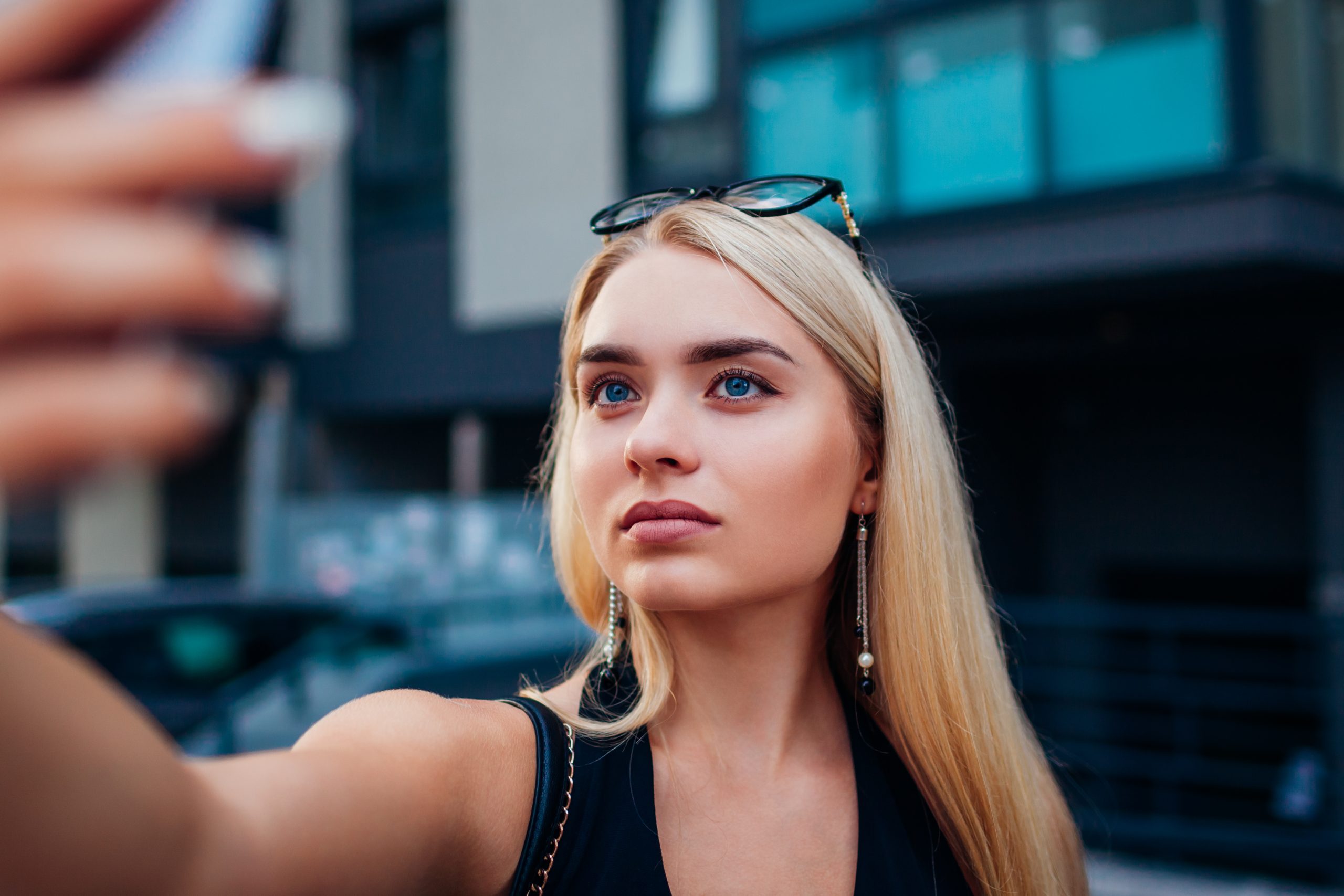 Beautiful young woman taking selfie while having orange juice in outdoor cafe. Stylish fashionable girl chilling on the street waiting for friends