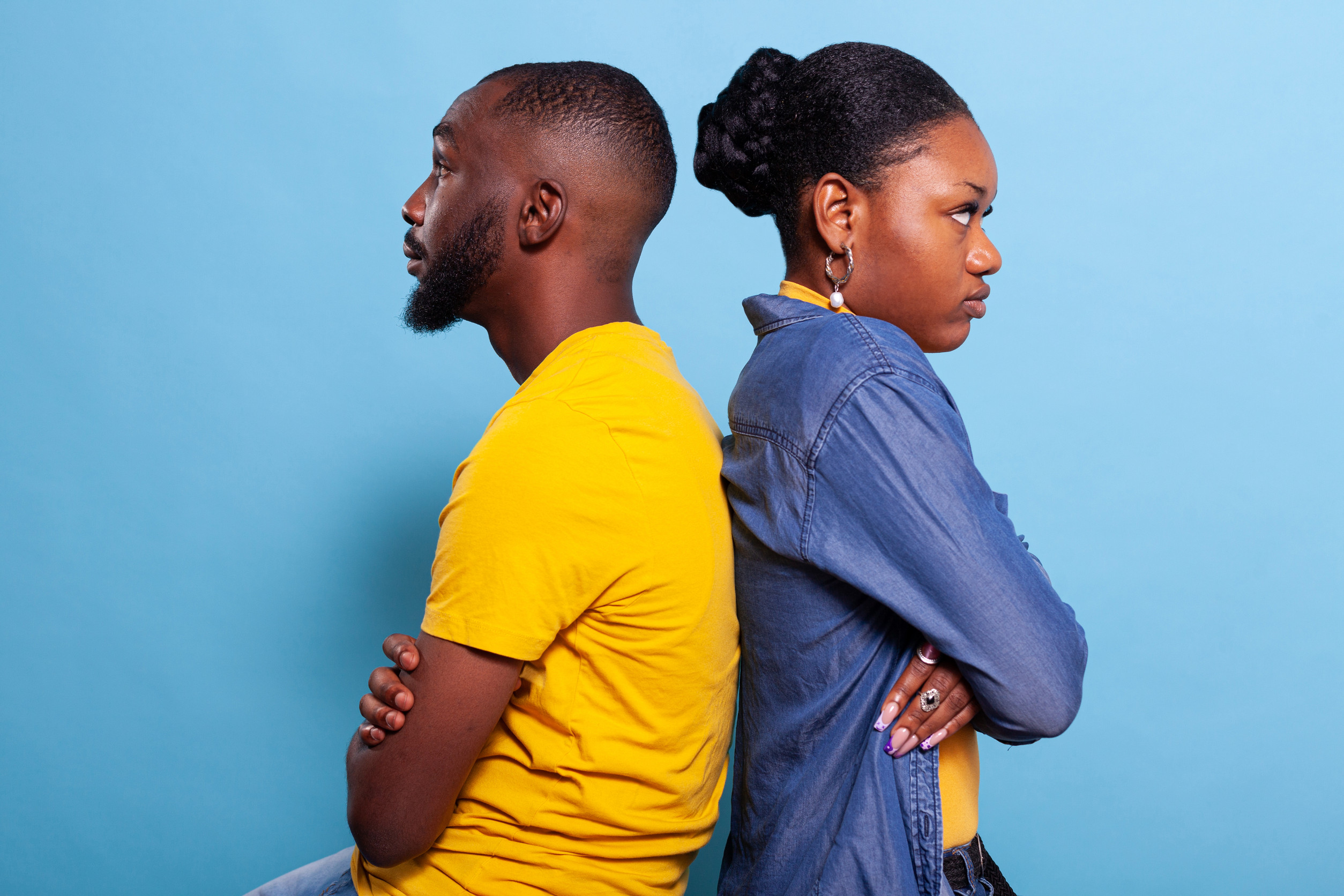 Angry partners sitting back to back with arms crossed in studio. Irritated boyfriend and girlfriend with relationship problems and argument fighting in front of camera. Distant upset couple