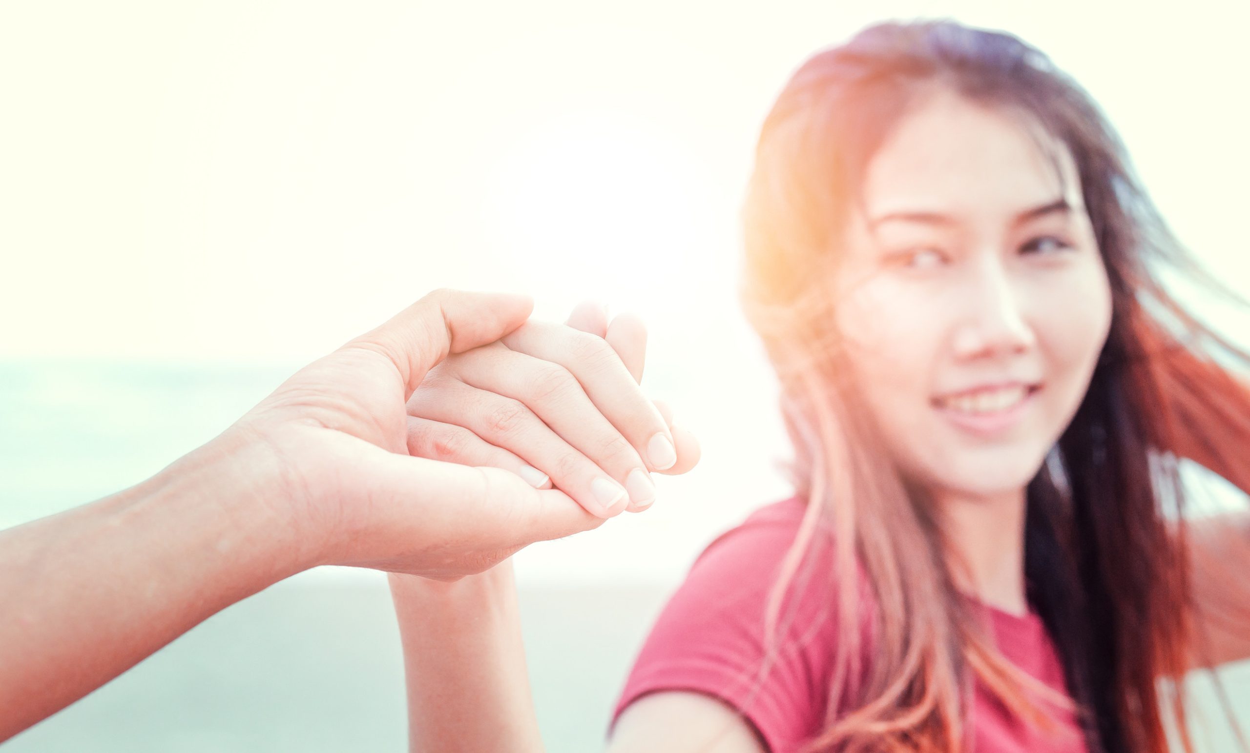 the man and the women hold one's hand on the beach and front of sunset.