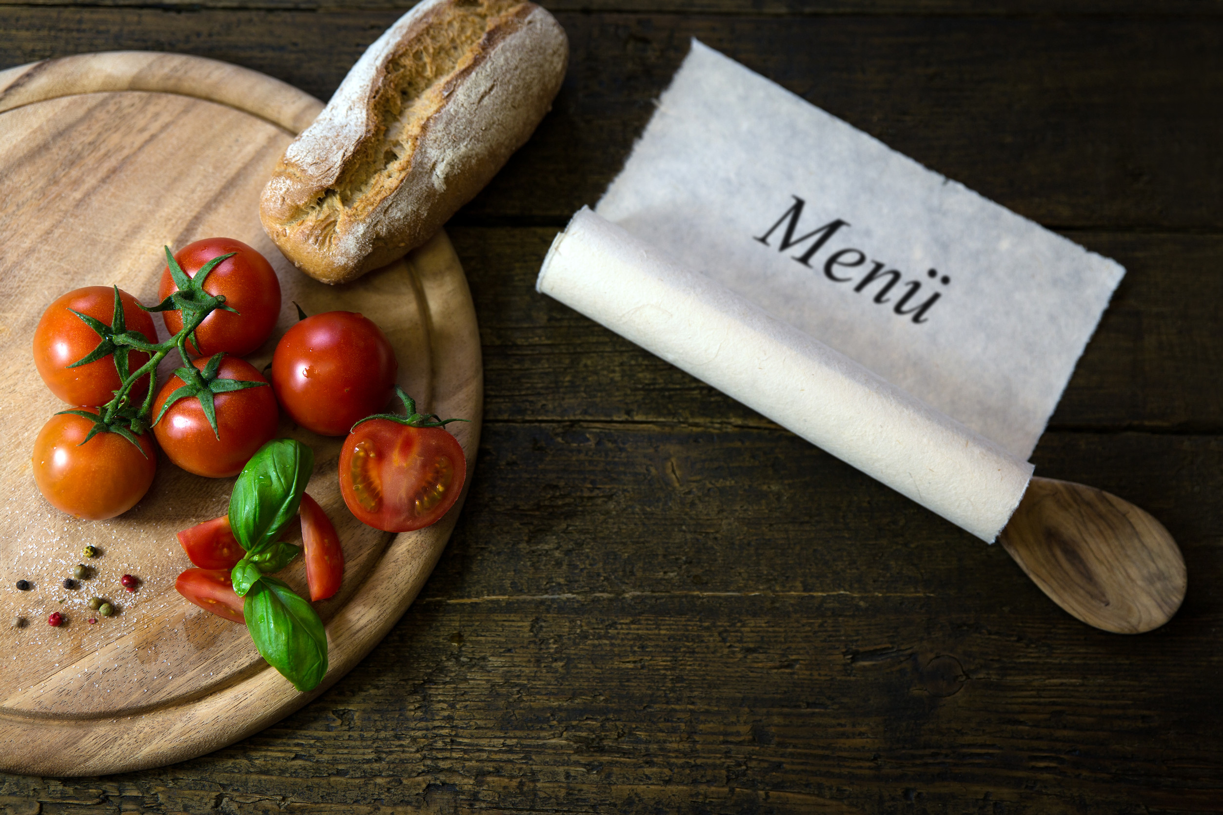 Tomatoes with basil and rustic bread on wooden table, scroll with german word menü